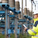 Energy business technology industry concept. Electrical engineer studying reading on tablet. Electrical worker engineer working with digital tablet near tower with electricity.